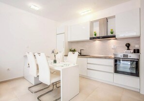 A modern kitchen with white cabinetry, a built-in oven, and a dining area with white chairs and a table.