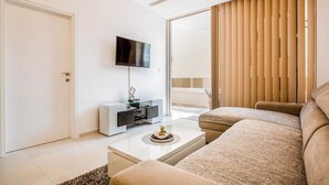 A modern living room with a flat-screen TV, a white entertainment unit, a beige sofa, and a glass coffee table.