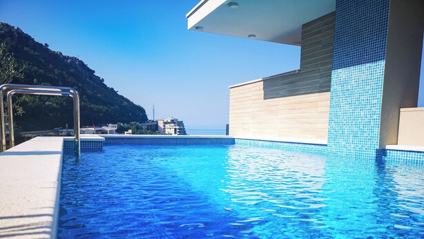 A swimming pool with clear blue water, a metal ladder, and a view of buildings and hills in the background.