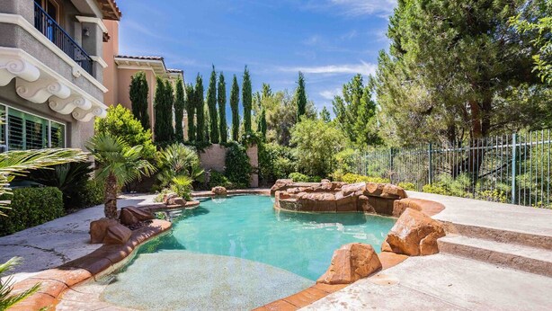A swimming pool with a stone border and steps leading into it, surrounded by greenery and a building with balconies. - Hacienda near the Las Vegas Strip (Las Vegas Nevada)