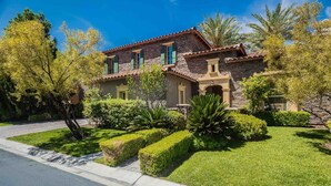 A two-story house with a stone facade, green shutters, and a well-maintained front yard with hedges and a palm tree. - Hacienda near the Las Vegas Strip (Las Vegas Nevada)