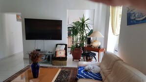 Un salon avec un canapé, une table basse, un téléviseur, une plante en pot et une lampe.