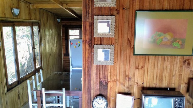 A wooden interior with a dining area, a refrigerator with magnets, a clock, and a television. - TerrazaMar EcoCabañas (Quintero)