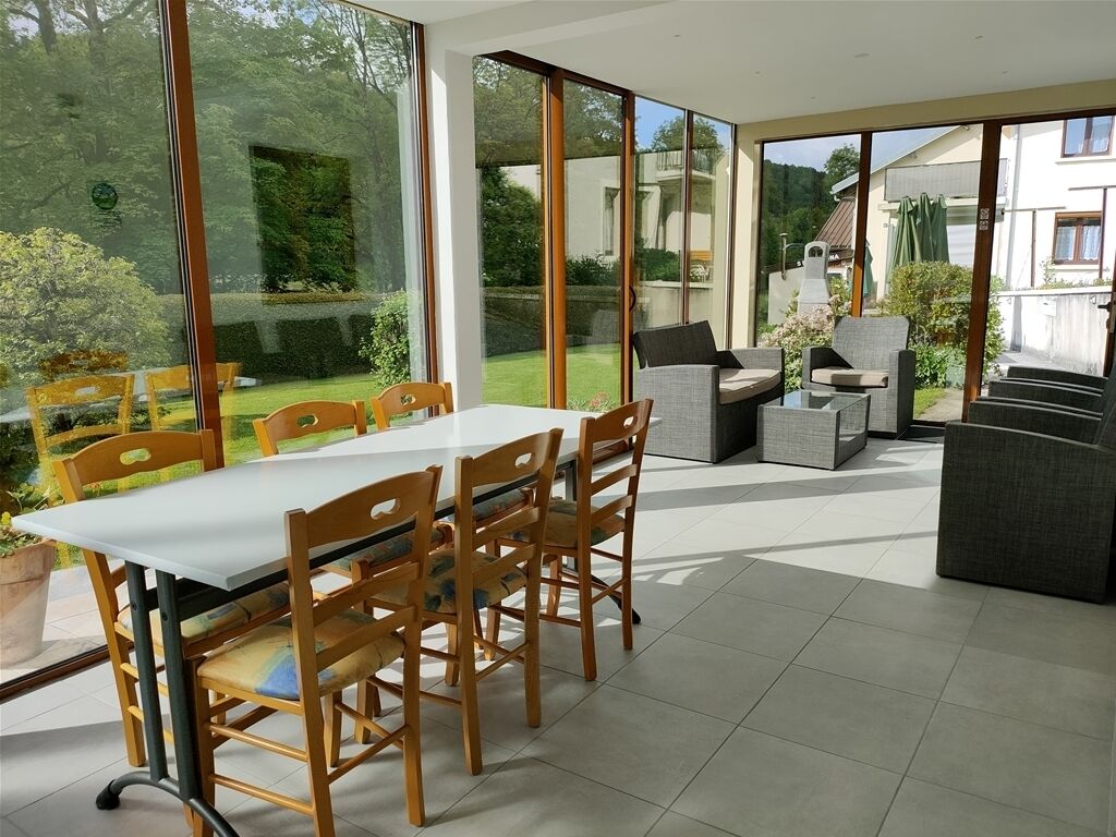 A spacious patio with a dining table and chairs, large sliding glass doors leading to a garden, and a barbecue area.