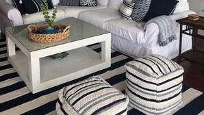 Ein modernes Wohnzimmer mit einem weißen Sofa, gestreiften Hocker und einem Glastisch.