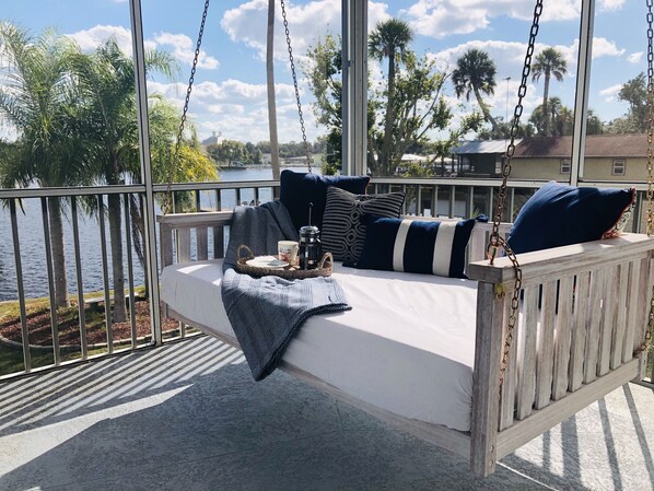 A wooden swing bed with a view of a lake and palm trees. - Luxury 5 Star Rated Homosassa Home.  Prime location, ultra-clean, well designed  (Homosassa)