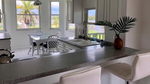 Eine moderne Küche mit weißen Schränken, einer Arbeitsplatte aus Granit und einem Essbereich mit weißen Stühlen.