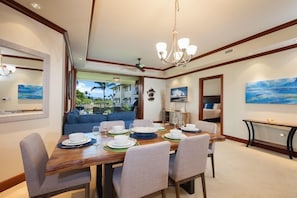 Comedor con una gran mesa de madera dispuesta para seis personas, una araña y vista a un paisaje tropical a través del ventanal.