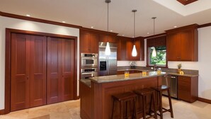 A modern kitchen with wooden cabinets, stainless steel appliances, a central island with stools, and pendant lighting. - Hilton Waikoloa Pool Pass thru 2026. Golf Discounts. Kolea 16B (Waikoloa Beach Resort)