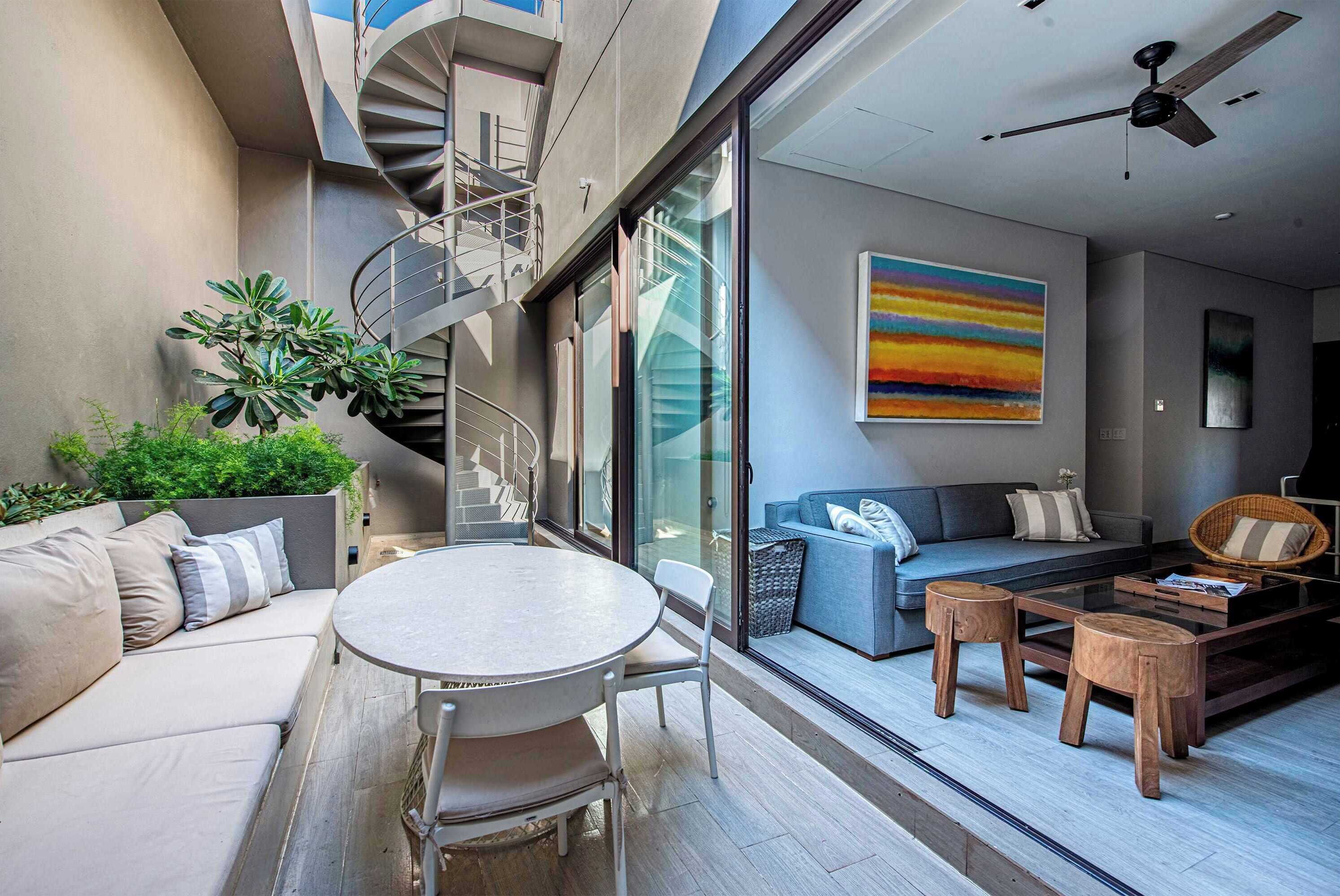 Un espace de vie moderne comprenant un escalier en colimaçon, un mur en verre, un canapé, une table basse et un tableau.