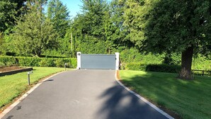 Ein gepflasterter Weg führt zu einem verschlossenen Eingang, umgeben von üppigem Grün und Bäumen.
