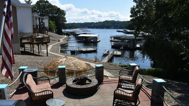 A patio with outdoor seating, a fire pit, and a view of a lake with boats. - Lakefront Retreat Sleeps 19 • Hot Tub + Paddle Boards • Family & Group Favorite! (Eldon)