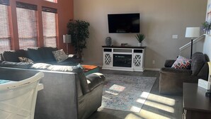 A living room with a sofa, a coffee table, a TV, and a ceiling fan. - Lakefront Retreat Sleeps 19 • Hot Tub + Paddle Boards • Family & Group Favorite! (Eldon)