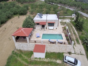 Ein zweistöckiges Steinhaus mit Pool, überdachter Terrasse und einem in der Nähe stehenden Auto.