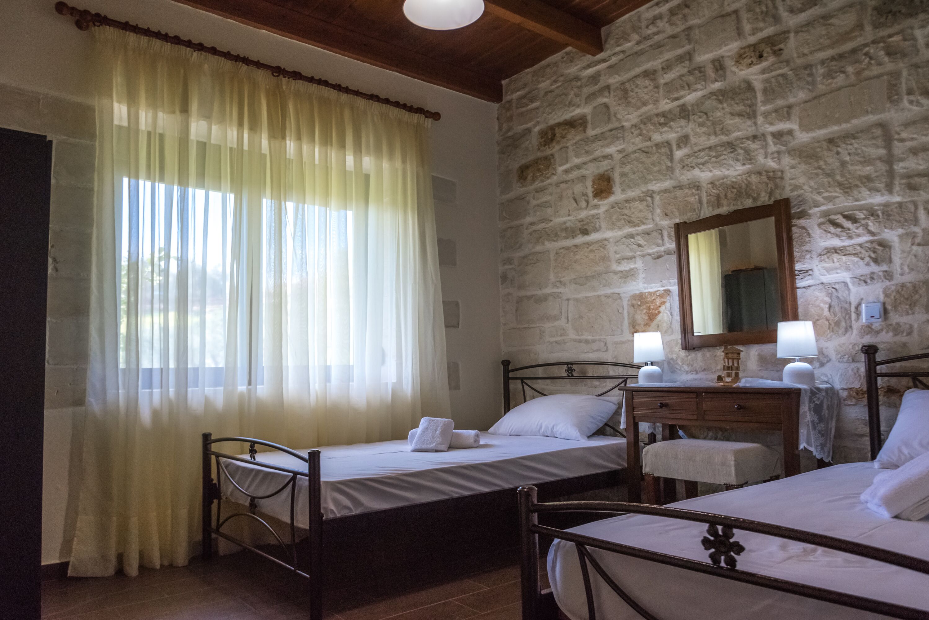 A bedroom with two beds, a wooden dresser, a mirror, and a stone wall.