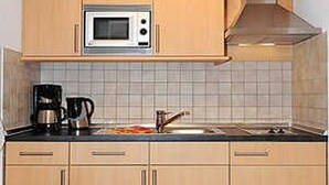 A kitchen with wooden cabinets, a microwave, a coffee maker, and a sink. - Apartment 16 - Castle Restaurant (Werdum)