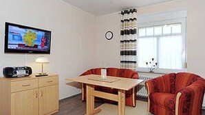 A living room with a TV, wooden cabinet, red sofa, and a dining table. - Apartment 16 - Castle Restaurant (Werdum)