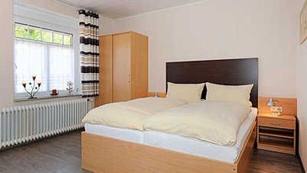 A bedroom with a wooden bed, a nightstand, a wardrobe, and a window with curtains. - Apartment 16 - Castle Restaurant (Werdum)