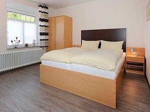 Quarto com cama de madeira, mesa de cabeceira, guarda-roupa e janela com cortinas.