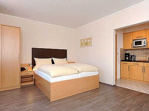 Quarto com cama de madeira, mesa de cabeceira, guarda-roupa e uma kitchenette com micro-ondas.