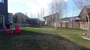 Ein Garten mit Trampolin, Holzzaun und einem Haus im Hintergrund.