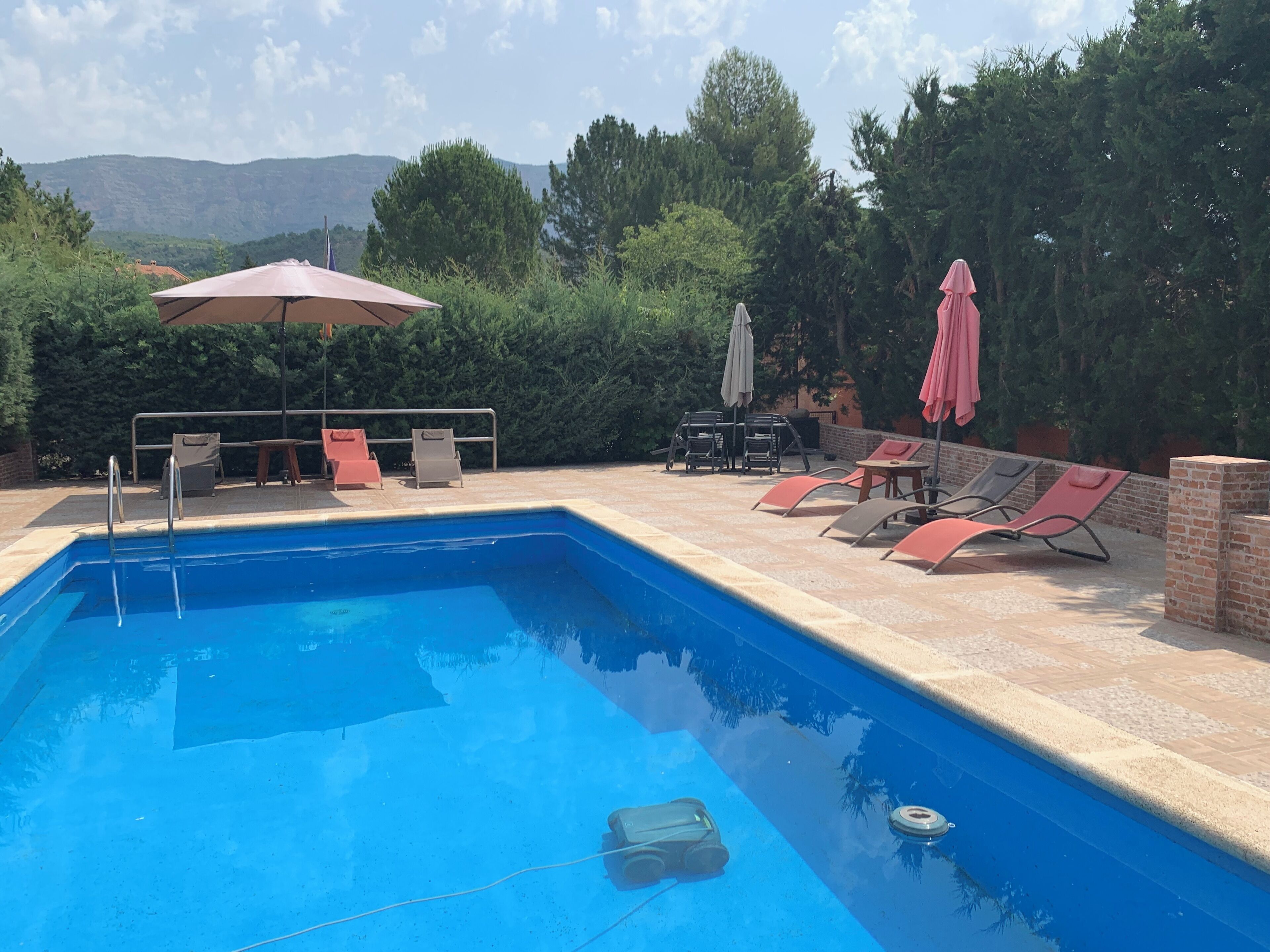 Une piscine entourée de verdure, avec des chaises longues et des parasols, d’où l’on peut admirer les collines lointaines.