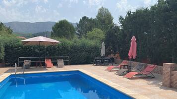 Une piscine entourée de verdure, avec des chaises longues et des parasols, d’où l’on peut admirer les collines lointaines.