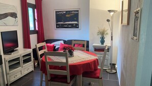 A cozy room with a bed, a TV, a dining table with chairs, and a small side table with a lamp.