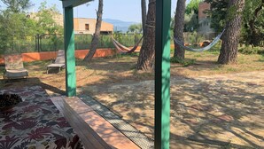 A covered outdoor area with a hammock, chairs, and a patterned tablecloth.