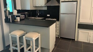 A modern kitchen with white cabinets, a stainless steel refrigerator, a black countertop, and two white stools.