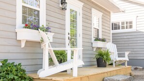 Une véranda avec des fauteuils Adirondack blancs et des jardinières remplies de fleurs.
