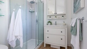 Une salle de bain moderne avec une douche à parois de verre, des meubles blancs et une petite étagère contenant des articles de toilette.