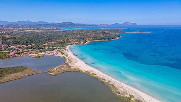 An aerial view of a coastal area with a beach, a small town, and surrounding hills.