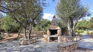 An outdoor stone-built pizza oven surrounded by trees in a landscaped area.