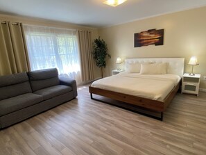 Relax in comfort with a large bed, sofa, and potted plant, surrounded by natural light and artwork.