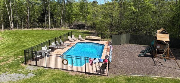 Relax by the pool surrounded by a lush lawn and a wooden play area for kids.