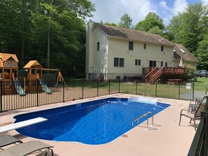 Relax by the pool surrounded by lush greenery and a wooden play structure for the kids.