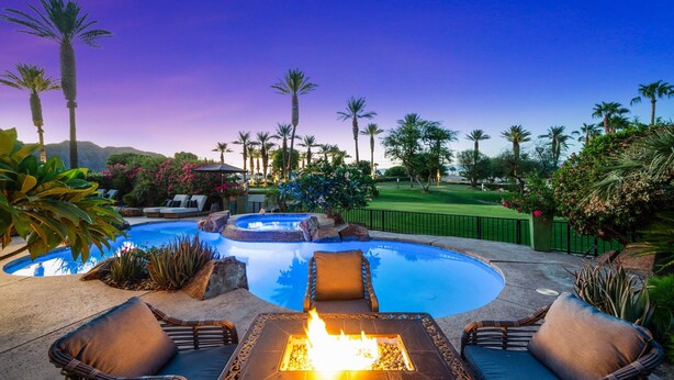 A pool area with lounge chairs and a fire pit, surrounded by palm trees and a well-maintained lawn. - Rancho La Quinta Country Club Spanish Beauty w/ Detached Casita  (La Quinta)