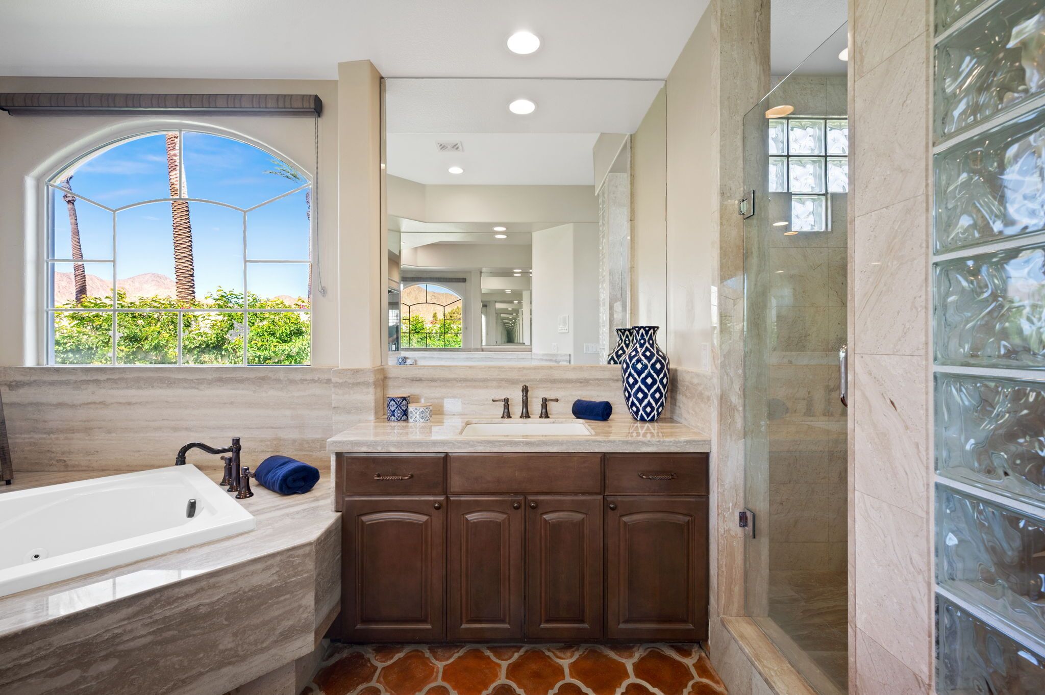A modern bathroom with a large bathtub, a walk-in shower, and a large window with a view of palm trees.