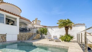 A clear swimming pool with a stone wall and a palm tree. - Vacation home Sunset by Interhome (Empuriabrava)