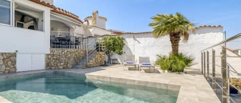 A clear swimming pool with a stone wall and a palm tree.
