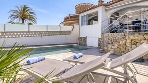 A pool area with lounge chairs and a stone wall. - Vacation home Sunset by Interhome (Empuriabrava)