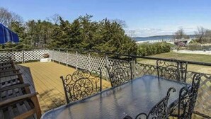 A deck with a view to the beach, featuring a table and chairs, surrounded by a fence. - Bayfront Vacation Home in Southold, 5 Bedrooms (Southold)