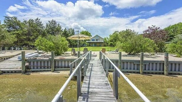 A wooden pier leading to a dock with a house in the background. - Bayfront Vacation Home in Southold, 5 Bedrooms (Southold)