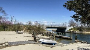 A sandy beach with a dock, a small boat, and a bridge over a body of water. - Bayfront Vacation Home in Southold, 5 Bedrooms (Southold)