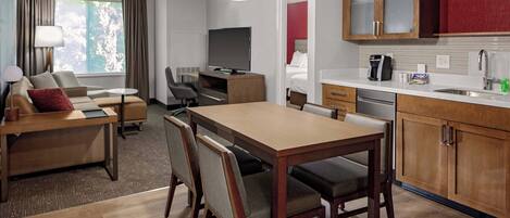A hotel room with a dining area, a TV, a sofa, and a kitchen with wooden cabinets.