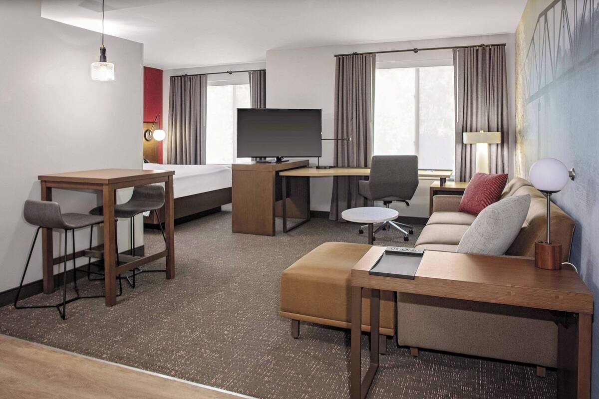 Una habitación de hotel con cama, escritorio con computadora, televisión, sofá y una pequeña mesa.