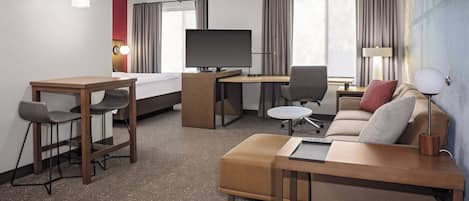 Una habitación de hotel con cama, escritorio con computadora, televisión, sofá y una pequeña mesa.