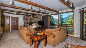A cozy living room with a stone fireplace, large windows with a mountain view, and a wooden ceiling. - The Cedars Luxury  At Windcliff 5 Bedroom Home by RedAwning (Estes Park)