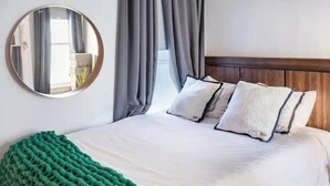 A neatly made bed with a green knitted throw, a round mirror on the wall, and a wooden headboard. - Walkable Urban Retreat - 2 En-Suite Baths - Near Top Dining & Shops & Hotspots! (SF)